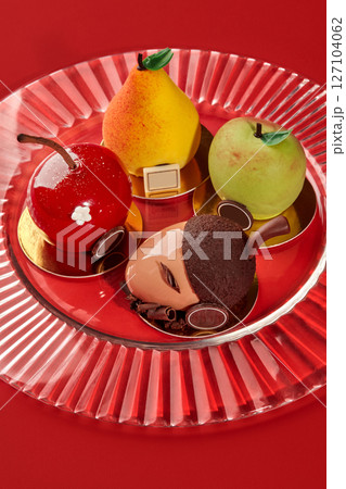 Delicious fruit shaped cakes resembling apple, pear, cherry and acorn on red plate 127104062