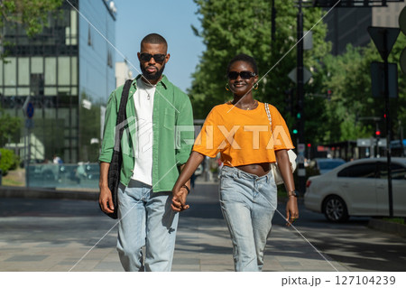 Pleased loving african american couple smiling walks in downtown together holding hands enjoy stroll 127104239