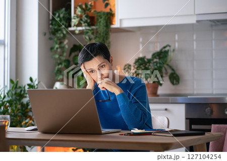 Exhausted burdened mature woman looks at laptop screen at home, with notebook of notes nearby Exhausted burdened mature woman looks at laptop screen at home, with notebook of notes nearby 127104254