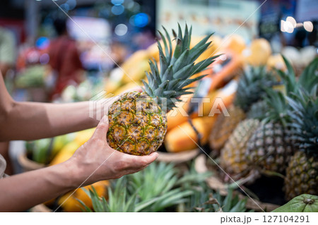 Tourist selects pineapple at market, hand holds fruit inspecting texture and color on street store 127104291