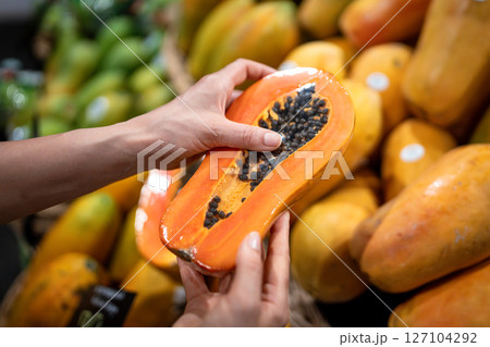 Hands checking papaya fruit freshness firmness, cutting halved fruit with seeds at street market Hands checking papaya fruit freshness firmness, cutting halved fruit with seeds at street market 127104292