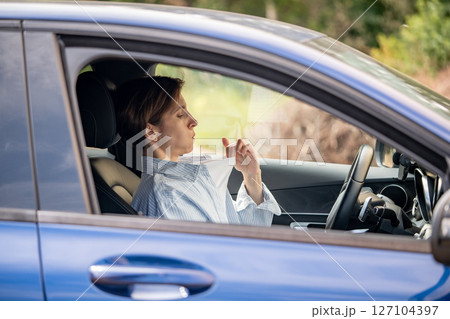 Woman driver sweating in heat blowing on chest, broken air conditioner in car in summer. 127104397