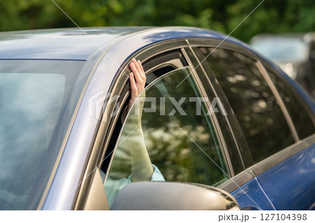 Woman checking hot weather temperature by sticking fingers out of slightly opened car window. 127104398