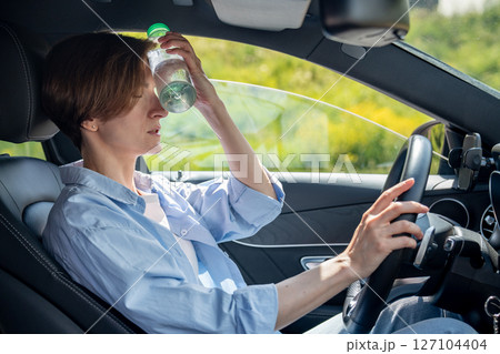 Hot weather for drivers. Tired from heat woman in car take break cooling forehead with cold bottle  127104404