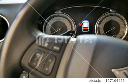 Car dashboard with illuminated open door icon behind defocused steering wheel 127104423