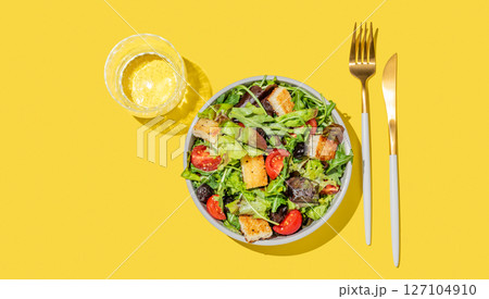 Vegetable salad with lettuce, tomatoes, croutons and olives in a bowl on a yellow background 127104910