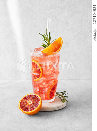 Blood orange cocktail with ice and rosemary on a marble stand on a gray background 127104921
