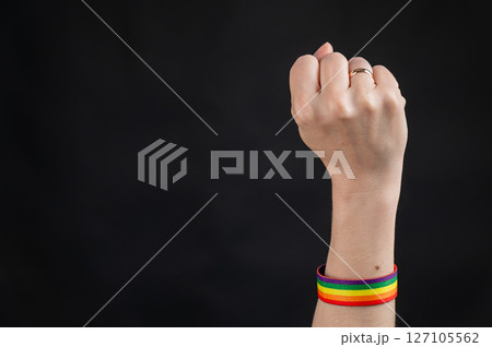 Woman with wedding ring and rainbow bracelet holding fist on black background. Woman with wedding ring and rainbow bracelet holding fist on black background. 127105562