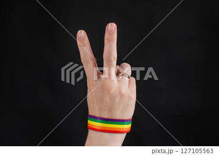Woman with wedding ring and rainbow bracelet holding palm on black background. Woman with wedding ring and rainbow bracelet holding palm on black background. 127105563