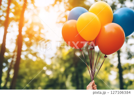 Vintage Style Photo of Hand Holding Colorful Balloons in a Sunlit Forest Setting 127106384