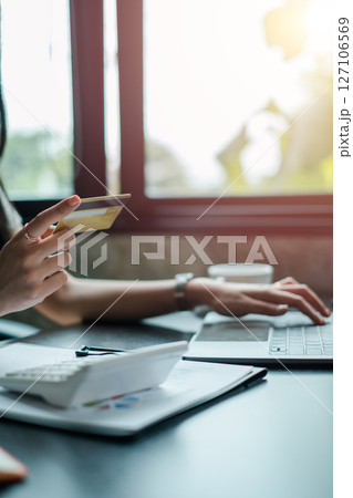 Close-up of a woman using a credit card and laptop for online shopping in a bright, modern setting. Close-up of a woman using a credit card and laptop for online shopping in a bright, modern setting. 127106569