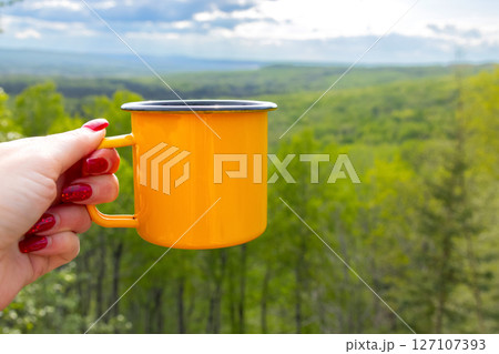 Hiker's female hand is holding a yellow camping cup. Hiker's female hand is holding a yellow camping cup. 127107393