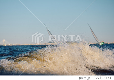 Sailing regatta in the Gulf of Finland at sunset, two sailing yachts competing in a race, splashing water from under the boats, teamwork, board the boat 127108574