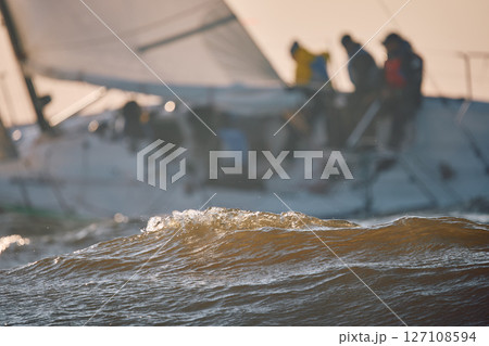 Sailing regatta in the Gulf of Finland at sunset, sailing yacht competing in a race, splashing water from under the boat, teamwork, board the boat Sailing regatta in the Gulf of Finland at sunset, sailing yacht competing in a race, splashing water from under the boat, teamwork, board the boat 127108594