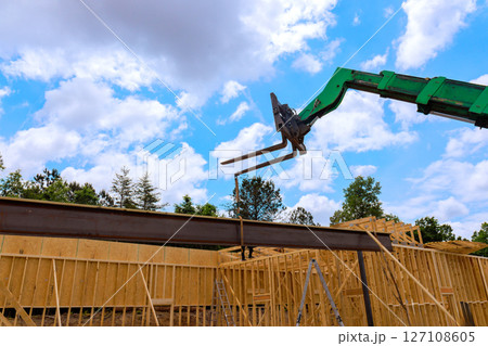 Heavy telehandler machinery lifts steel beam at construction site surrounded by wooden frames 127108605