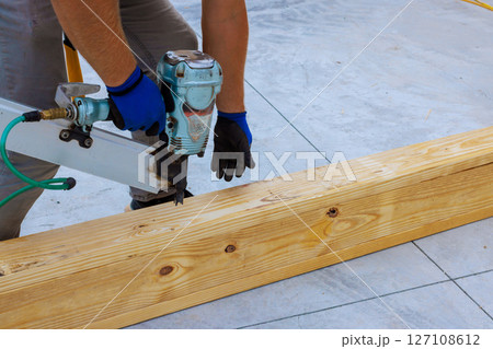 Craftsman focuses on nailing wooden beams together at construction site using pneumatic nail gun Craftsman focuses on nailing wooden beams together at construction site using pneumatic nail gun 127108612