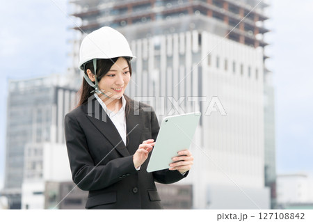 スーツにヘルメット被ってタブレットを操作する若い女性　施工管理者　現場監督　土木女子（ドボジョ） 127108842