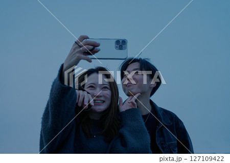 夕闇が迫る海岸で写真を撮る若い男女 夕闇が迫る海岸で写真を撮る若い男女 127109422