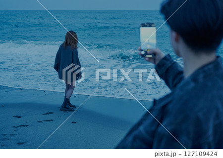 夕闇が迫る海岸で写真を撮る若い男女 夕闇が迫る海岸で写真を撮る若い男女 127109424
