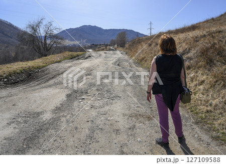 A woman on a dirt mountain road leading to a village in the Altai Mountains in spring 127109588