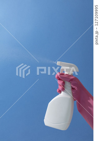 A spray bottle is held up against a clear blue sky by a pink-gloved hand, turning an everyday cleaning moment into a fun, creative visual. A spray bottle is held up against a clear blue sky by a pink-gloved hand, turning an everyday cleaning moment into a fun, creative visual. 127109995