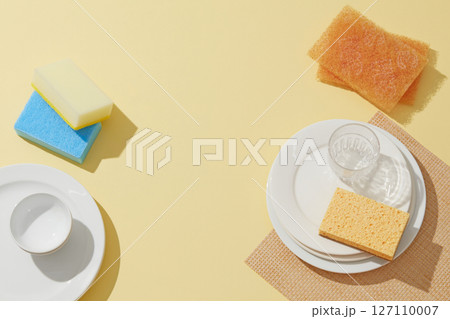 A dish washing sponge, scrubber, and detergent bottle arranged neatly on a yellow plate, creating a concept of kitchen hygiene and dish-cleaning essentials. Blank space for design 127110007