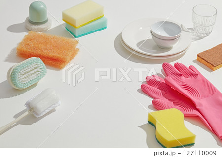 Colorful sponges, brushes, and gloves placed beside a few dishes, highlighting household cleaning essentials in a well-lit kitchen space. Copy space 127110009