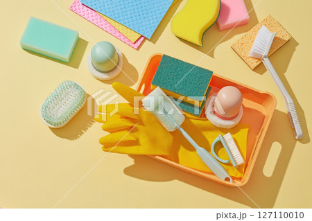 Multiple scrubbing pads, gloves, sponges and spray bottles scattered across a vibrant yellow surface, evoking energy and cleaning activity. Cleaner concept Multiple scrubbing pads, gloves, sponges and spray bottles scattered across a vibrant yellow surface, evoking energy and cleaning activity. Cleaner concept 127110010