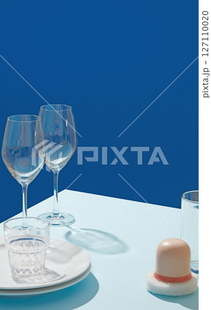 Blue background still life featuring clear wine glasses and pastel-colored cleaning props, showcasing dish care and refined aesthetics. Blank space for presentation product Blue background still life featuring clear wine glasses and pastel-colored cleaning props, showcasing dish care and refined aesthetics. Blank space for presentation product 127110020