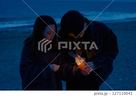 夜の海岸で手持ち花火をする若い男女 127110041