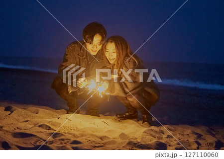 夜の海岸で手持ち花火をする若い男女 127110060