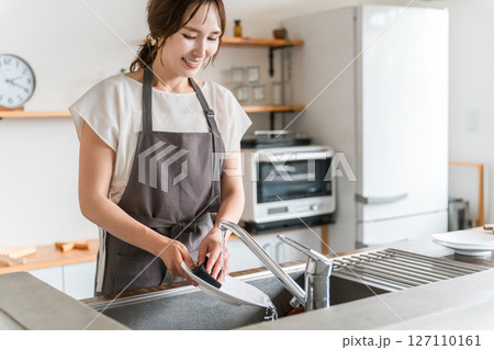 キッチンのシンクで洗い物,皿洗いをするエプロン姿の主婦 キッチンのシンクで洗い物,皿洗いをするエプロン姿の主婦 127110161