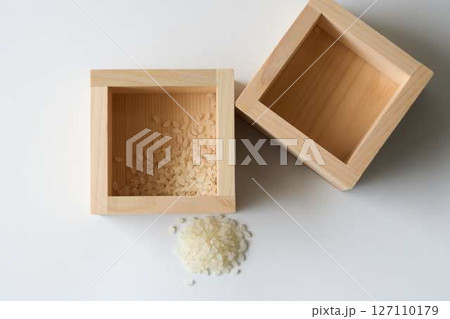 白背景に少しのコメが入った升とこぼれたコメ 127110179