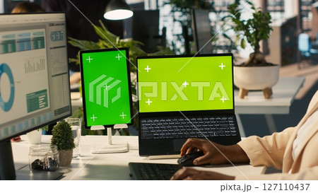 Mockup tablet and laptop in office used by employee working on company administrative tasks. Chroma key devices on desk used by worker reviewing business data metrics, camera A 127110437