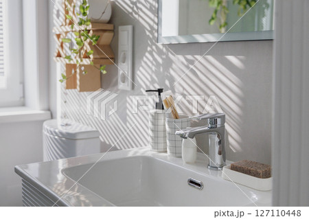 Stylish clean white bathroom with light gray tiles on the walls and lots of indoor plants. 127110448