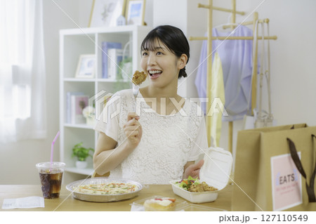 デリバリーで頼んだ食べ物を置いた食卓の前で唐揚げを食べようとする座る若い女性 デリバリーで頼んだ食べ物を置いた食卓の前で唐揚げを食べようとする座る若い女性 127110549