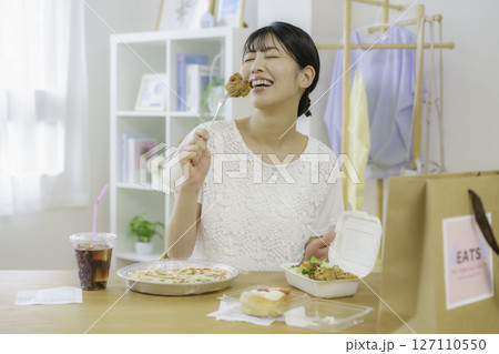 デリバリーで頼んだ食べ物を置いた食卓の前で唐揚げを食べようとする座る若い女性 デリバリーで頼んだ食べ物を置いた食卓の前で唐揚げを食べようとする座る若い女性 127110550
