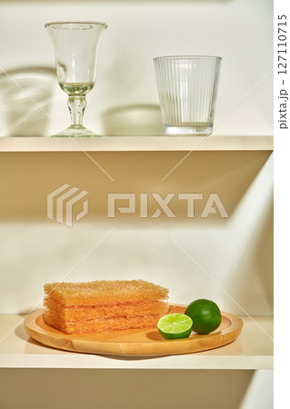 Sponges are stacked next to two glasses on a shelf. Soft lighting highlights a quiet kitchen corner with a clean and cozy atmosphere. advertising cleaning products with green lemon ingredients Sponges are stacked next to two glasses on a shelf. Soft lighting highlights a quiet kitchen corner with a clean and cozy atmosphere. advertising cleaning products with green lemon ingredients 127110715