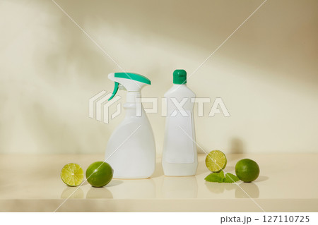 Spray bottles and cleaners are placed next to fresh lemons and mint leaves. The image combines the fresh scent of citrus with everyday cleaning supplies. 127110725
