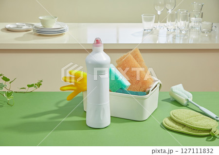 A bottle of dishwashing liquid next to a tray of brushes and cloths, all on a green surface, underlining freshness and kitchen care essentials. A bottle of dishwashing liquid next to a tray of brushes and cloths, all on a green surface, underlining freshness and kitchen care essentials. 127111832