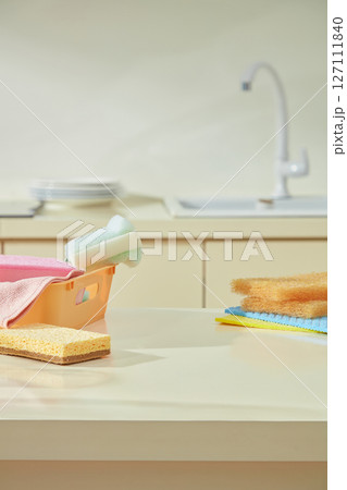 Kitchen cleaning tools with colorful towels and sponges placed on the kitchen island. In the background is the sink and cleaned dishes. 127111840