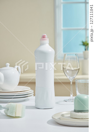 Close-up of a white bottle and ceramic plates neatly arranged on a beige surface, surrounded by soft window light and pastel tones. Kitchen dishwashing and cleaning products Close-up of a white bottle and ceramic plates neatly arranged on a beige surface, surrounded by soft window light and pastel tones. Kitchen dishwashing and cleaning products 127111841