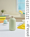 On a minimalist kitchen background with many tools for cleaning the kitchen, a green product bottle without label is placed in the center, no label for branding design, kitchen cleaning products 127111859