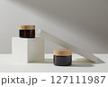 Front view of twp amber cosmetic jars unlabeled decorated with white podiums on a white background. Minimal scene for advertising cosmetic product with space for design label 127111987