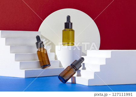 On contrasting color background, red and blue background, white geometries podiums displayed with three amber serum bottles. Container packaging of skin care branding On contrasting color background, red and blue background, white geometries podiums displayed with three amber serum bottles. Container packaging of skin care branding 127111991