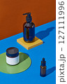 Empty and unlabeled cosmetic bottle decorated with colored platform on contrasting orange and blue background. Scene for product presentation, object placement, cosmetic podium template 127111996