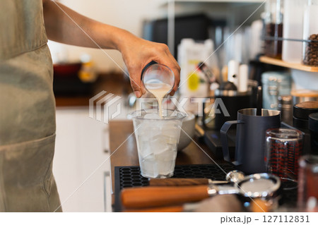 Woman barista preparing coffee latte pouring milk into a glass with iced. Woman barista preparing coffee latte pouring milk into a glass with iced. 127112831