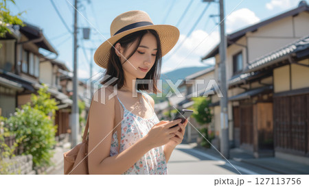 伝統的な町並みでスマートフォンを操作する麦わら帽子の女性 127113756