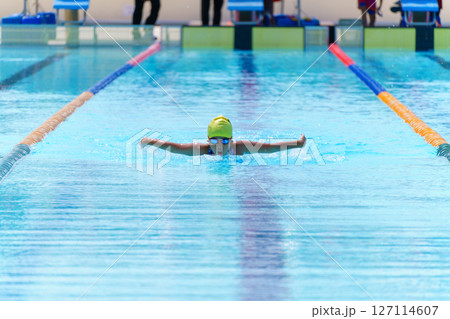 Swimmer child swims butterfly swimming style in a race swimming pool. Water sports and competition, learning to swim classes for children. Swimmer child swims butterfly swimming style in a race swimming pool. Water sports and competition, learning to swim classes for children. 127114607