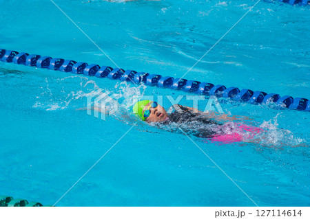 Swimmer child swims backstroke swimming style in a race swimming pool. Water sports and competition, learning to swim classes for children. 127114614